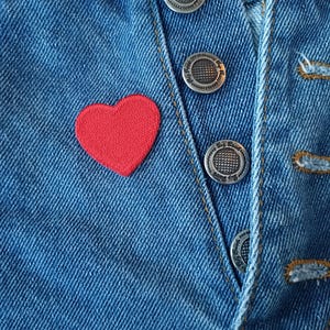 May include: A red heart-shaped patch sewn onto a blue denim jacket with silver buttons.