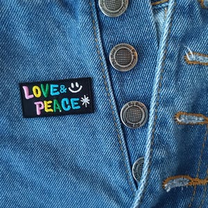 May include: A blue denim jacket with a colorful embroidered patch that says "LOVE & PEACE" with a smiley face. The jacket has silver metal buttons.