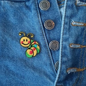 May include: A blue denim jacket with a smiling yellow caterpillar patch. The patch has red, green, and blue details.