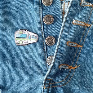 May include: A blue denim jacket with silver buttons and a small train patch on the front.
