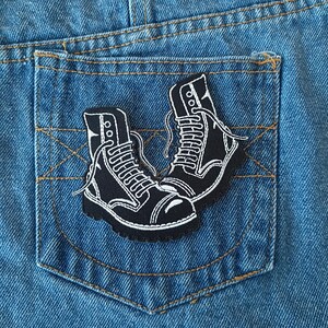 May include: Black and white embroidered patch of two boots on a blue denim background.