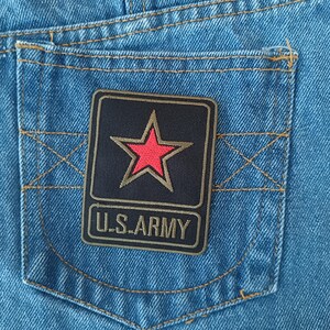May include: Close-up of a light blue denim pocket with a black patch. The patch features a red star within a gold outline, and the text "U.S. ARMY" in gold lettering.