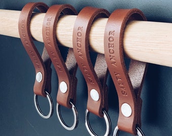 May include: Four brown leather keychains with silver key rings. Each keychain has the text "Salty Anchor" embossed on it.