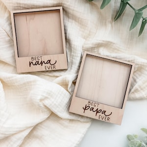 May include: Two wooden photo frames with a light wood grain. One frame reads "BEST nana EVER" and the other reads "BEST papa EVER" in a cursive font. The frames are square with a black border.