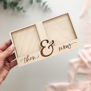 May include: A light-colored wooden photo frame with two rectangular openings. The frame features the words "then & now" in a decorative font. The ampersand symbol is prominently displayed in a darker wood tone.