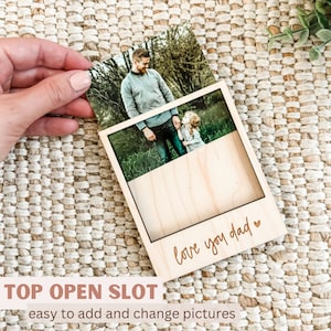 May include: A wooden photo frame with a top opening slot for inserting photos. The frame has a light wood finish and the words "love you dad" are engraved on the front.