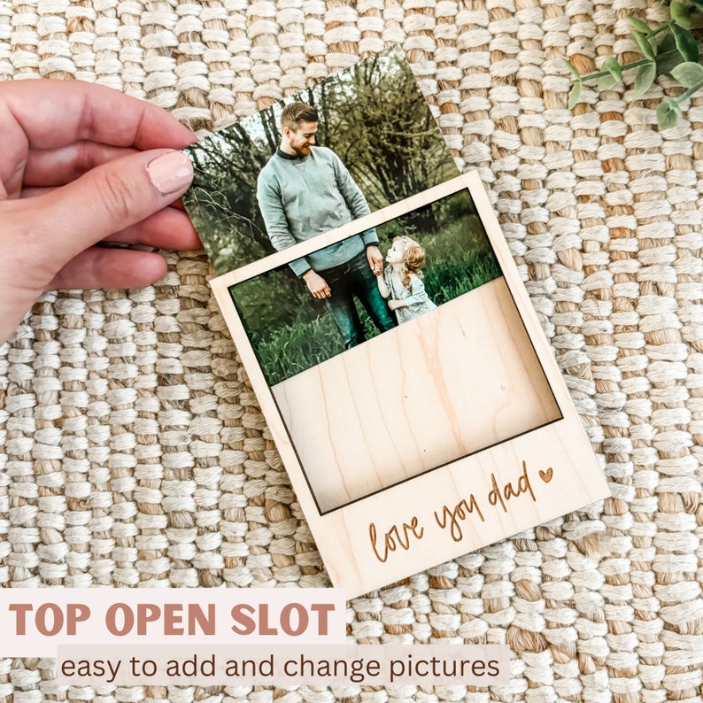 May include: A wooden photo frame with a top opening slot for inserting photos. The frame has a light wood finish and the words "love you dad" are engraved on the front.