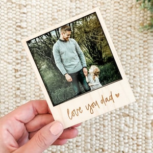 May include: A wooden photo frame with a picture of a father and daughter in a forest. The frame has a light brown wood finish and the text "love you dad" is engraved on the bottom.