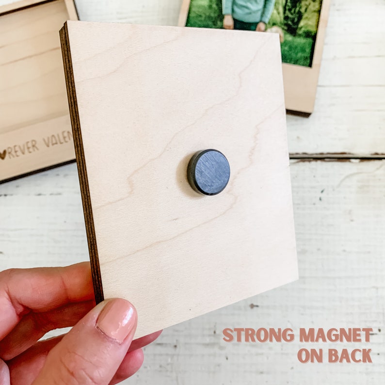 May include: A wooden photo frame with a strong magnet on the back. The frame is light brown and has a smooth surface. The magnet is black and round.
