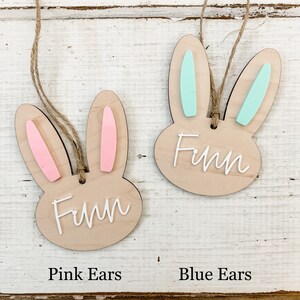 May include: Two wooden bunny ornaments with the name Finn written on them. One bunny has pink ears and the other has blue ears.