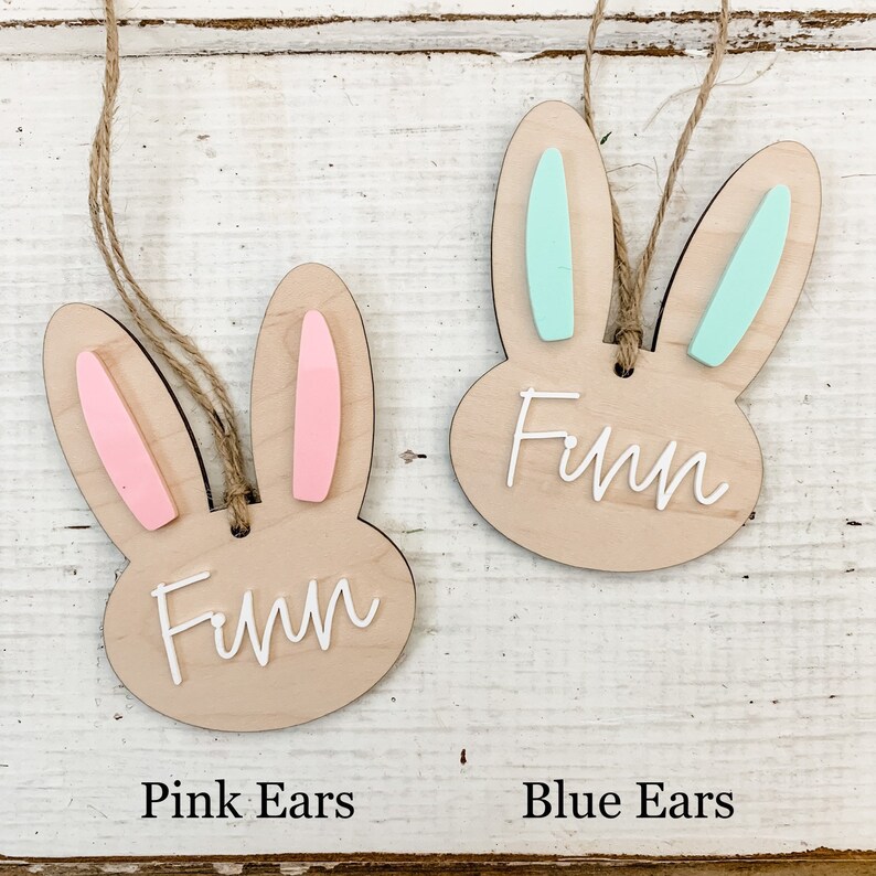 May include: Two wooden bunny ornaments with the name Finn written on them. One bunny has pink ears and the other has blue ears.