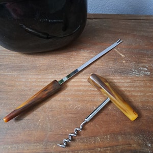 May include: A vintage brown and gold corkscrew with a metal worm and a wooden handle. A matching brown and gold bottle opener with a metal prong is also pictured.