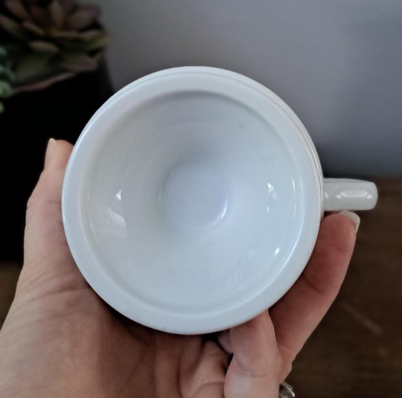 May include: A white ceramic teacup with a simple design. The cup is empty and has a small handle.