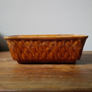 May include: A brown ceramic planter with a diamond pattern. The planter is rectangular and has a slightly raised rim.