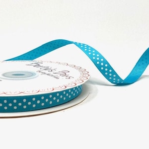 May include: A spool of turquoise blue ribbon with white polka dots. The ribbon is on a white spool with a label that says "The Ribbon Bar".