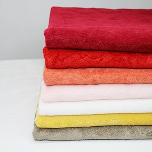 May include: A stack of six towels in various colors, including red, orange, pink, white, yellow, and brown. The towels are folded and stacked neatly on a white surface.