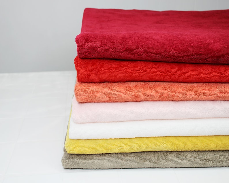 May include: A stack of six towels in various colors, including red, orange, pink, white, yellow, and brown. The towels are folded and stacked neatly on a white surface.