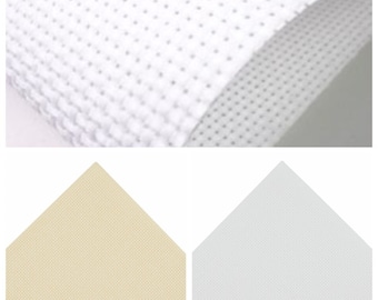 Puede incluir: Dos muestras de tela Aida blanca, una de color crema y otra de color blanco. La tela es un tejido tejido con pequeños agujeros, comúnmente utilizado para el bordado de punto de cruz.