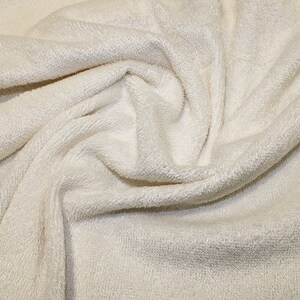 May include: Close-up of a soft, white, textured fabric. The fabric has a slightly fuzzy appearance and is folded in a way that shows its texture.