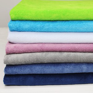 May include: A stack of seven towels in various colors, including green, blue, white, pink, gray, and two shades of blue. The towels are folded and stacked neatly.