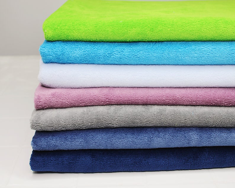 May include: A stack of seven towels in various colors, including green, blue, white, pink, gray, and two shades of blue. The towels are folded and stacked neatly.