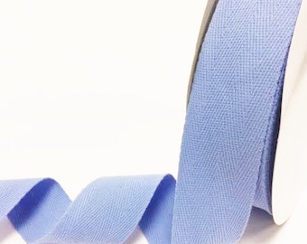 May include: A roll of light blue cotton twill tape with a herringbone pattern. The tape is 1 inch wide.
