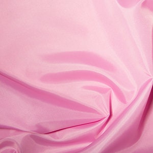 May include: Close-up of a pink fabric with a shiny, smooth texture. The fabric is gathered and folded, creating shadows and highlights that emphasise its soft, flowing nature. The colour is a light, pastel pink.