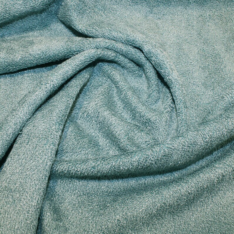 May include: A close-up of a soft, textured, teal-colored fabric. The fabric is folded and draped, showing its texture and color.