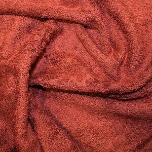 May include: Close-up of a red, textured fabric with a soft, fuzzy surface. The fabric is folded and wrinkled, creating a variety of textures and patterns.