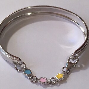 Pu&ograve; includere: Un braccialetto rigido in argento con una catena di quattro ciondoli smaltati. I ciondoli hanno la forma di stelle e sono di colore blu, rosa e giallo.