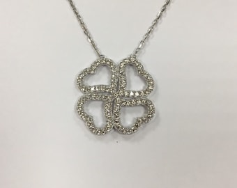 Puede incluir: Un collar de plata con un colgante de trébol de cuatro hojas hecho de corazones entrelazados. El colgante está engastado con pequeños diamantes transparentes.
