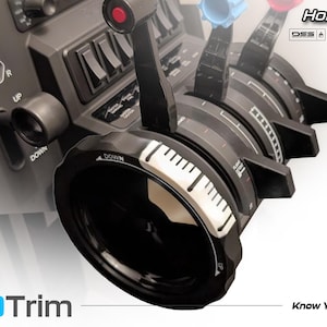 Może przedstawiać: Panel sterowania symulatorem lotu AeroTrim z wieloma dźwigniami, pokrętłami i przełącznikami. Koło trymowania jest czarne z białymi oznaczeniami. Widoczny jest tekst "Honeycomb Bravo TRIM WHEEL".