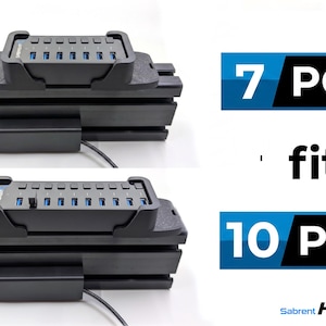 May include: A black plastic mounting bracket holding a Sabrent USB hub, shown in two configurations. The text reads 7 PORT fits 10 PORT and Sabrent HUBTECH. The bracket features a grooved design and is designed to secure the hub in place.