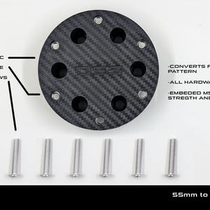 May include: A black carbon fiber wheel adapter with six silver screws. The adapter converts from 55mm to 70mm and includes embedded MS hardware and nuts. The text on the image says "MOZA ES" and "55mm to UNIVERSAL 70 mm WHEEL ADAPTER."