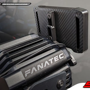 May include: A black Fanatec sim racing motor base with a carbon fiber textured mounting bracket attached to the top. The unit features a black metal housing with cooling fins and the white text Fanatec printed on the front. A thin black cable runs across the top of the motor housing.