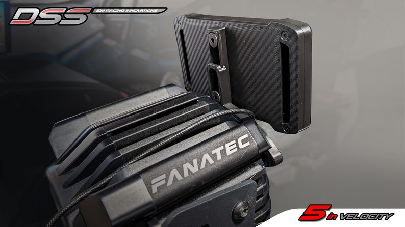 May include: A black Fanatec sim racing motor base with a carbon fiber textured mounting bracket attached to the top. The unit features a black metal housing with cooling fins and the white text Fanatec printed on the front. A thin black cable runs across the top of the motor housing.