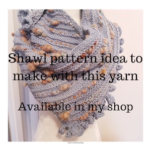 Op de afbeelding: Een grijze gebreide sjaal met een textuurpatroon en bruine garenakcenten. De sjaal heeft een gerimpelde rand en is over een mannequin gedrapeerd. De tekst "Shawl pattern idea to make with this yarn Available in my shop" is op de afbeelding gedrukt.