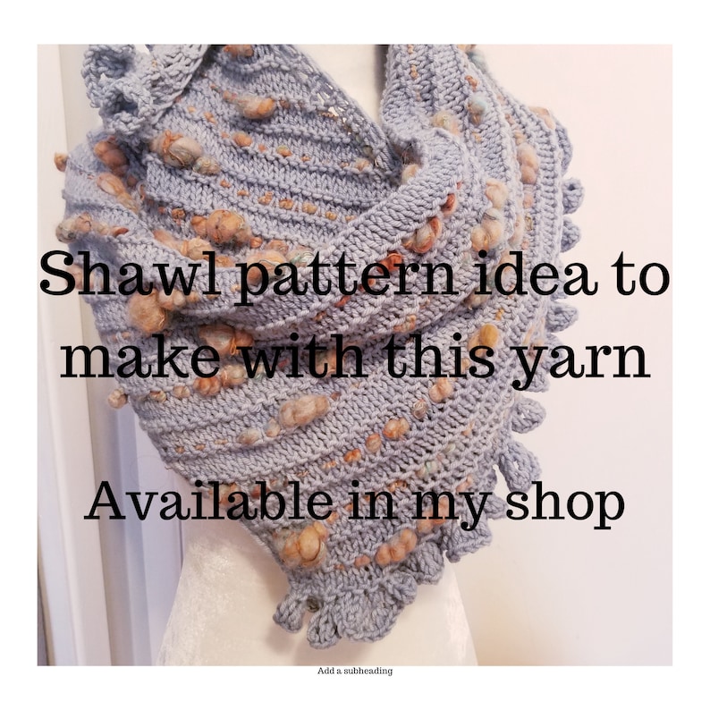 Op de afbeelding: Een grijze gebreide sjaal met een textuurpatroon en bruine garenakcenten. De sjaal heeft een gerimpelde rand en is over een mannequin gedrapeerd. De tekst "Shawl pattern idea to make with this yarn Available in my shop" is op de afbeelding gedrukt.