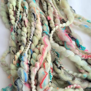May include: A skein of hand-dyed yarn in a pale green colour with multi-coloured accents. The yarn is made up of a variety of fibres, including wool, silk, and cotton. The yarn is perfect for knitting or crocheting.