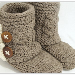 May include: A pair of brown knitted slipper boots with white crocheted trim and wooden buttons. The boots have a cable knit pattern.
