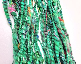 May include: A bundle of green, white, and multi-colored yarn with a variety of textures. The yarn is arranged in a loose, flowing pattern.