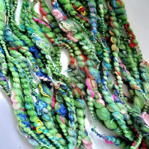 May include: Close-up of hand-spun yarn in shades of green, blue, pink, and red. The yarn is thick and textured, with a variety of colors woven throughout. The yarn appears to be made of wool or a similar fiber, and is suitable for knitting or other fiber arts projects.
