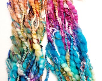 May include: A colorful assortment of hand-dyed yarn in shades of pink, orange, yellow, blue, and green. The yarn is arranged in a loose pile, showing the different textures and colors.