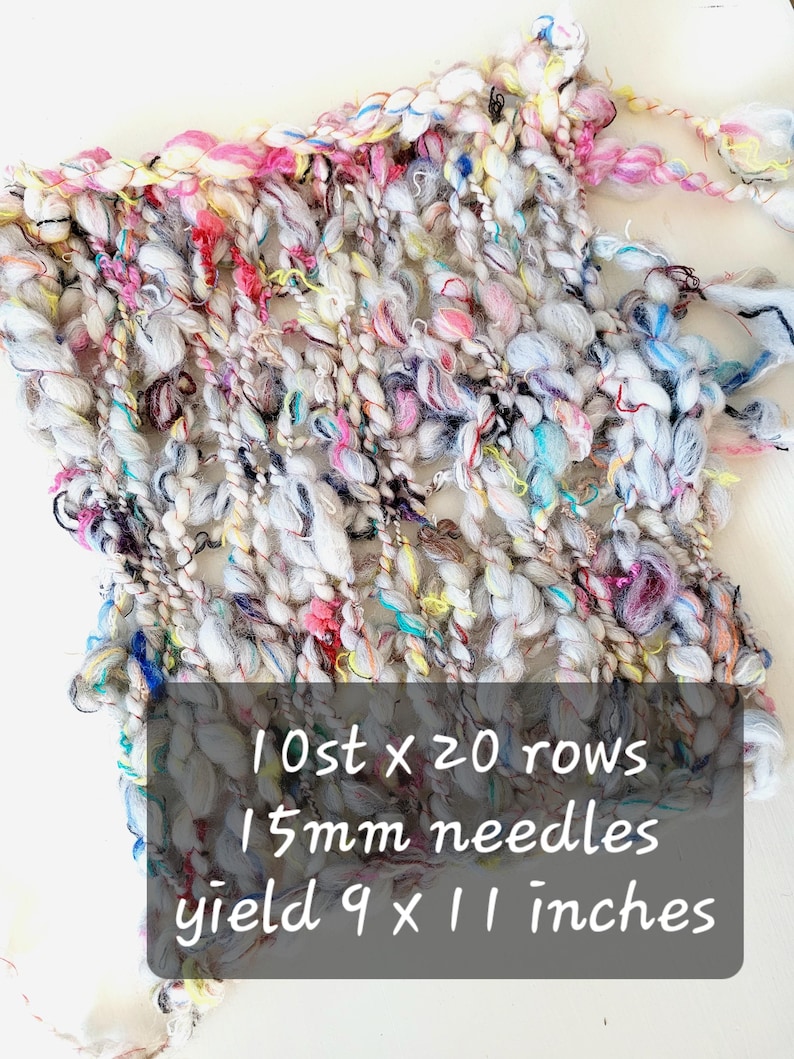 Op de afbeelding: Een kleurrijke gebreide stof met een witte basis en meerkleurige draden. De stof is 9 inch bij 11 inch en is gemaakt met 15 mm naalden. De tekst op de afbeelding luidt "10 st x 20 rijen 15 mm naalden opbrengst 9 x 11 inch".