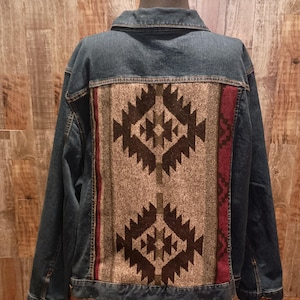 May include: A denim jacket with a patterned back panel. The back panel features a geometric design in shades of brown, gray, and burgundy. The jacket has a classic collar, button closures, and pockets. The jacket is displayed on a mannequin.
