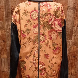 May include: A denim jacket with a floral pattern on the back. The jacket is a dark blue denim with a light brown floral pattern. The jacket has a collar and long sleeves.