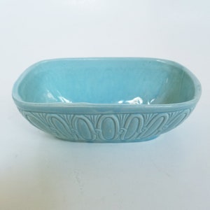 May include: A light blue ceramic bowl with a rectangular shape and rounded corners. The bowl features a decorative embossed pattern around the rim. The interior of the bowl is a solid light blue color.