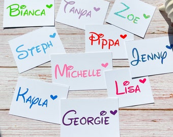 May include: Ten white cards with different names written on them in colourful, glittery letters. Each name has a small pink heart next to it. The names are Bianca, Tanya, Zoe, Steph, Pippa, Jenny, Michelle, Lisa, Kayla, and Georgie.