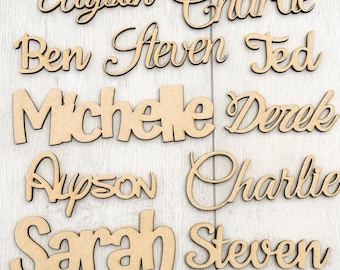 May include: A collection of wooden name cutouts in various cursive and block fonts. Names include Alyson, Charlie, Ben, Steven, Ted, Michele, Derek, Ayson, Sarah, and Steven. The cutouts are made of light brown wood.