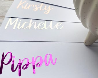 May include: Five white place cards with gold and silver foil lettering. The names on the cards are: Pippa, Michelle, Kirsty, Charlene, and Leanne.